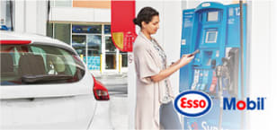 Photo d’une femme devant une pompe à essence avec les logos Esso et Mobil.